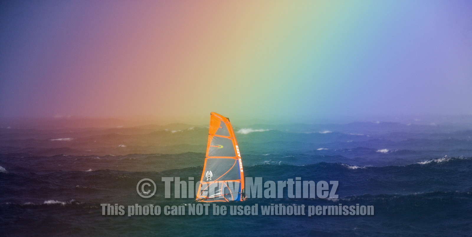 07_00208 ©ThMartinez. MAUI, HAWAII - USA, 6 January  2007 . .Sailing in the rainbow, a windsurfer in waves at Ho'okipa beach, North Shore of Maui Island (Hawaii-USA), as it's raining ...